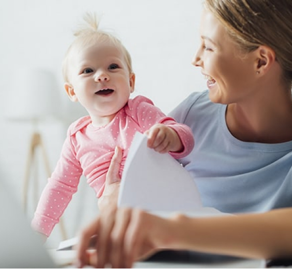 A woman is holding a baby while working on a laptop.